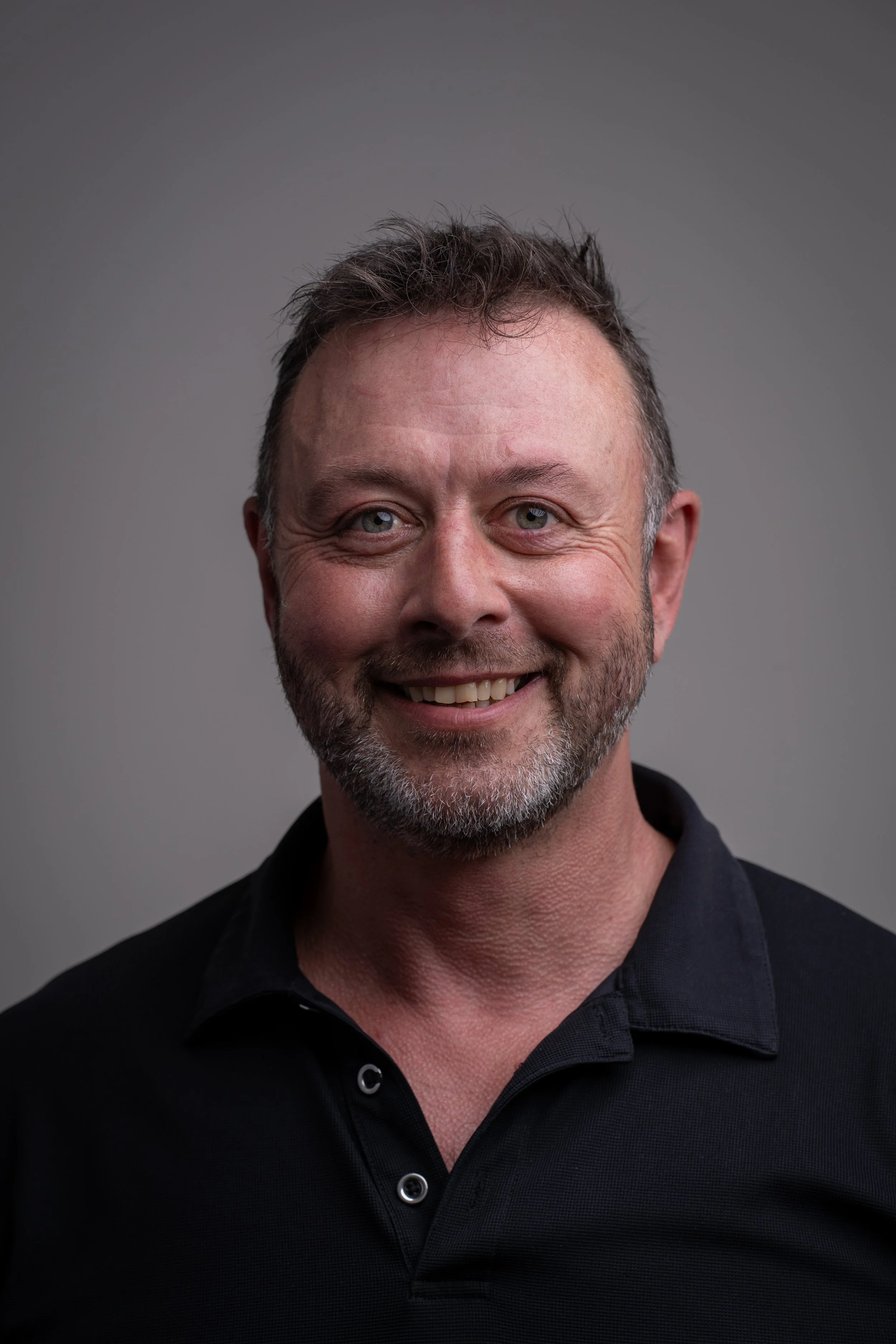 Portrait of James Aitken, an editorial and commercial photographer in Devon. He is a middle-aged man with brown hair and a beard, wearing a black t-shirt