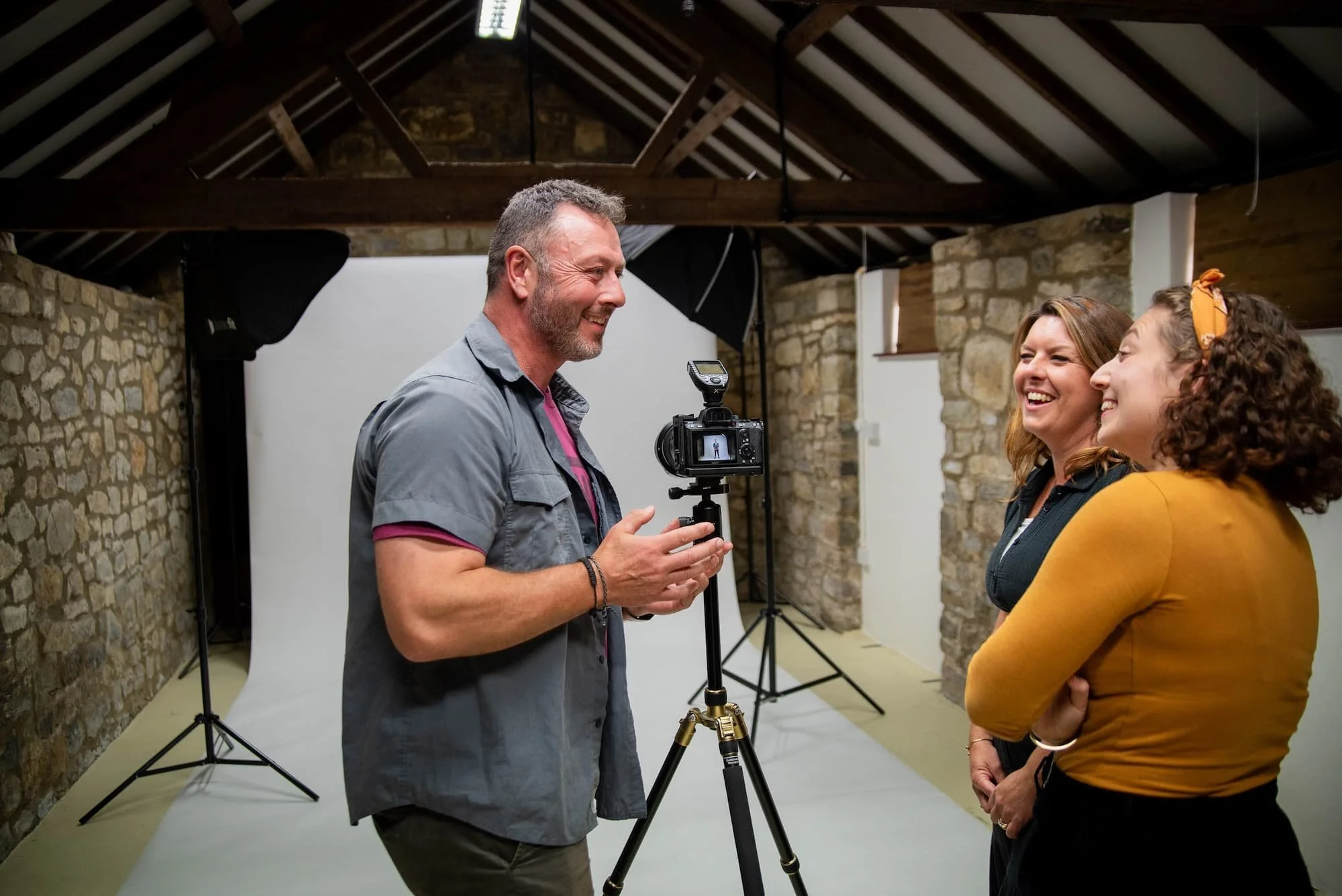Behind the scenes: James Aitken talking with two business professionals in a mobile photography studio, with a white backdrop and lighting set up behind them